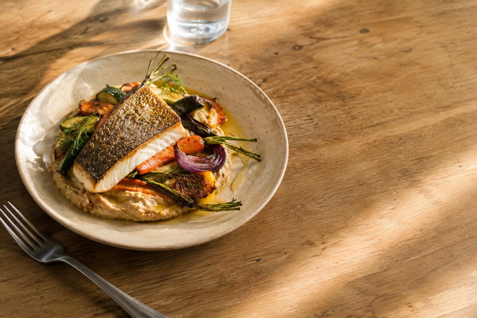 Une assiette Hormonia : poisson rôti, légumes de saison et purée de légumineuses, sur une table en bois.